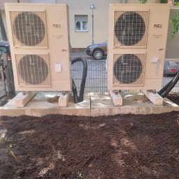 MKDienstleistungen Sp. z o.o. - Dwie jednostki zewnętrzne klimatyzacji typu split, ustawione na betonowych podstawach w ogrodzie, z widocznymi przewodami i świeżo przekopaną ziemią wokół.