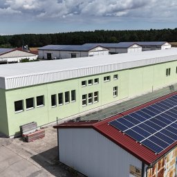 MKDienstleistungen Sp. z o.o. - Zielony budynek z panelami słonecznymi na dachu, widok z góry. W tle inne budynki z panelami i las. Na pierwszym planie komin z malowidłami.