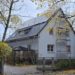 MKDienstleistungen Sp. z o.o. - Dom jednorodzinny z panelami słonecznymi na dachu, otoczony rusztowaniem. Jesienne liście na drzewach i chodniku. Widoczny fragment ogrodzenia i wejścia.