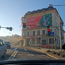 Adrian Maksymilian - Budynek z reklamą restauracji Good & One w Karpaczu, widziany z wnętrza samochodu na skrzyżowaniu. Czerwone światło sygnalizacji świetlnej. Słoneczny dzień.