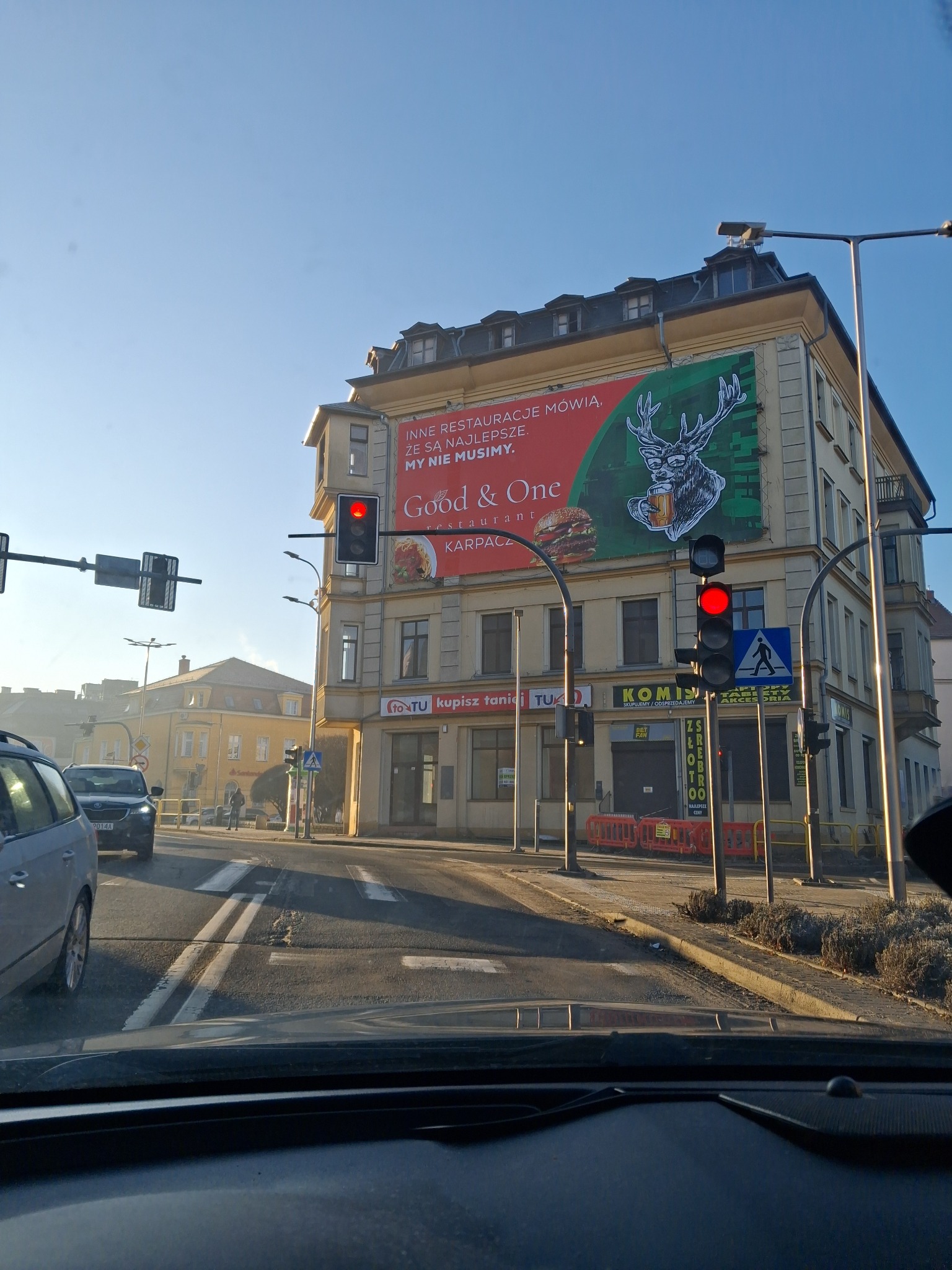 Budynek z reklamą restauracji Good & One w Karpaczu, widziany z wnętrza samochodu na skrzyżowaniu. Czerwone światło sygnalizacji świetlnej. Słoneczny dzień.