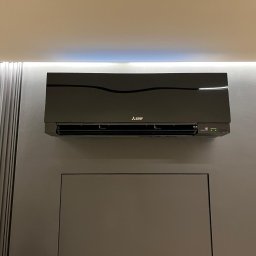 KlimatFix - Czarny klimatyzator Mitsubishi Electric na szarej ścianie z dekoracyjnymi panelami i oświetleniem LED. Nowoczesny design, widoczne diody sygnalizacyjne.