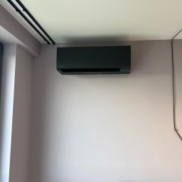 KlimatFix - Czarny klimatyzator Toshiba zamontowany na ścianie w pokoju w Warszawie. Widoczne czarne szyny sufitowe i fragment wezgłowia łóżka. Ściana w odcieniach fioletu.