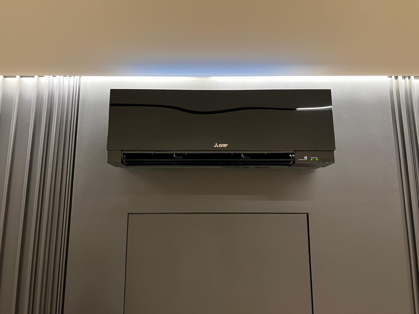 Czarny klimatyzator Mitsubishi Electric na szarej ścianie z dekoracyjnymi panelami i oświetleniem LED. Nowoczesny design, widoczne diody sygnalizacyjne.