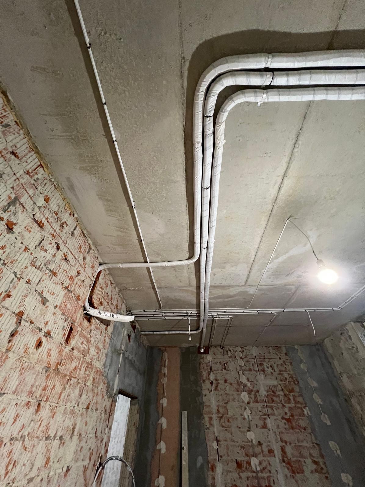 Montaż instalacji chłodniczej z izolacją termiczną na surowym suficie w pomieszczeniu z odsłoniętą cegłą. Widoczne rury i przewody.