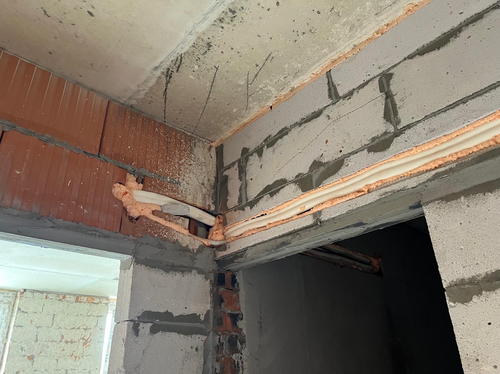 Montaż rur klimatyzacji w surowym wnętrzu, zabezpieczonych pianką montażową, widoczne cegły i beton. Instalacja w trakcie prac wykończeniowych.