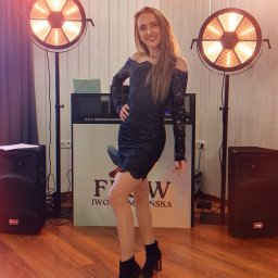 FLOW Iwona Smolińska - Uśmiechnięta kobieta w koronkowej sukience pozuje między dwoma reflektorami na statywach. W tle sprzęt muzyczny i logo firmy.