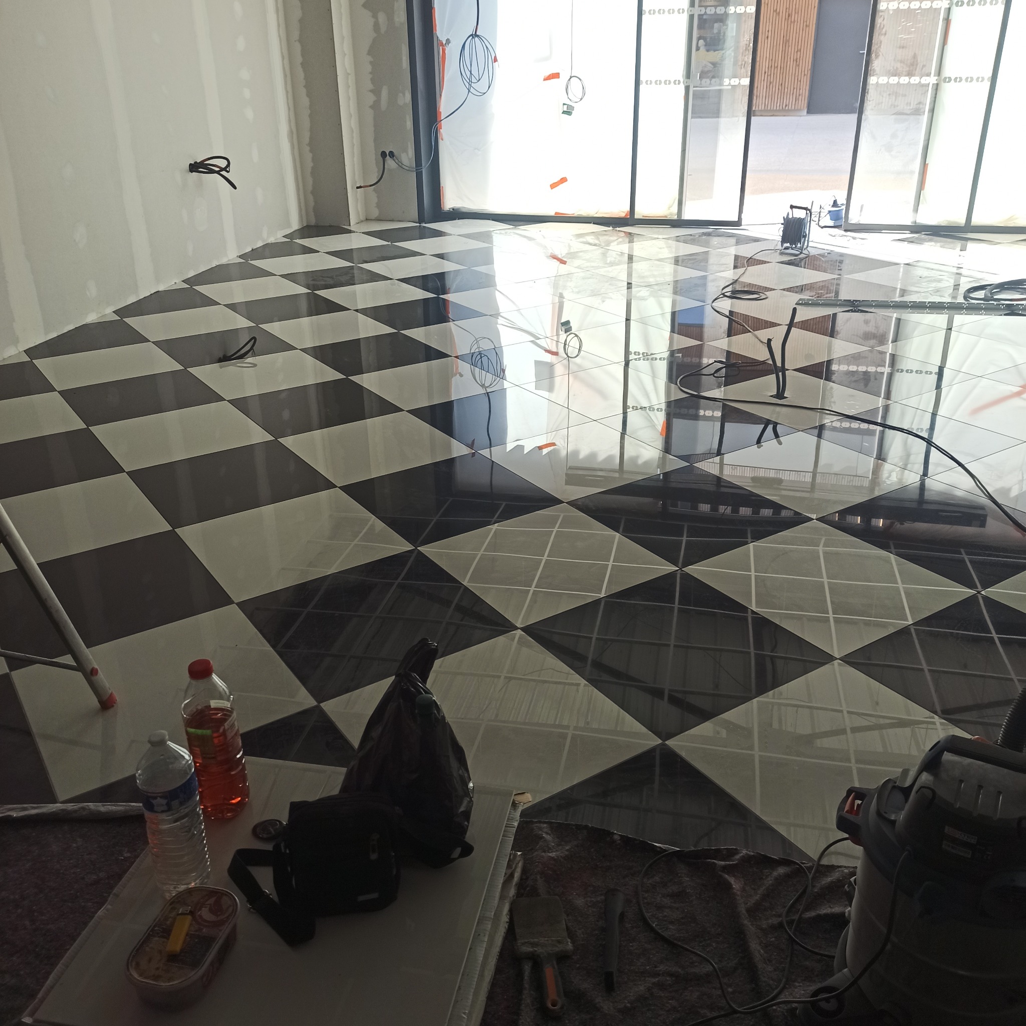 Ukończona podłoga z czarno-białych płytek ułożonych w karo, widoczne narzędzia i akcesoria glazurnicze, ściany przygotowane do dalszych prac wykończeniowych.