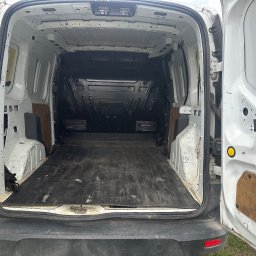 Tomasz Simlat - Wnętrze paki białego, brudnego busa z otwartymi drzwiami, widok z tyłu. Pusta przestrzeń ładunkowa z czarną podłogą i widocznymi śladami użytkowania.