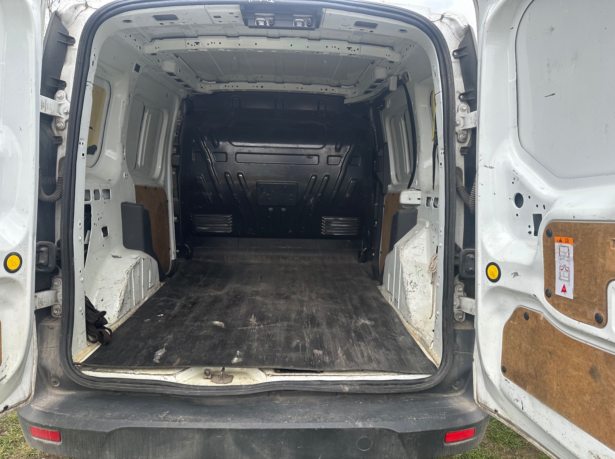 Wnętrze paki białego, brudnego busa z otwartymi drzwiami, widok z tyłu. Pusta przestrzeń ładunkowa z czarną podłogą i widocznymi śladami użytkowania.