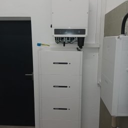 SejA EnergyL - Biała instalacja fotowoltaiczna z inwerterem i bateriami, zamontowana w pomieszczeniu. Widoczne kable i złącza. Minimalistyczny design.