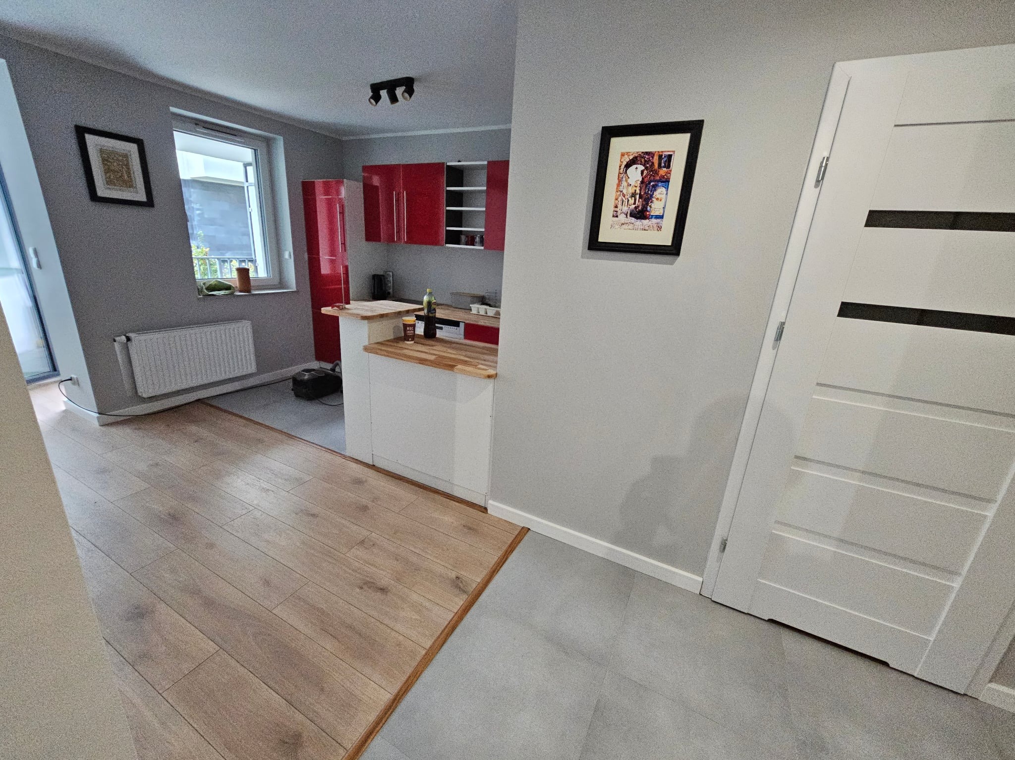 Wykończona kuchnia z czerwonymi szafkami i drewnianym blatem w Opolu. Widoczna podłoga z paneli i szara podłoga w kuchni. Na ścianie wisi obraz w czarnej ramie.