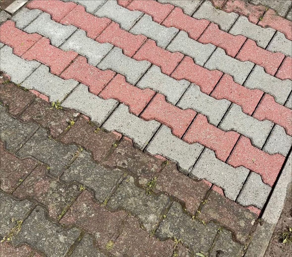 Częściowo wyczyszczona kostka brukowa w odcieniach szarości i czerwieni, widoczne różnice w kolorze i czystości, diagonalne ułożenie kostki.