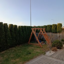 Czysty Błysk Anna Ostaszewska - Zadbany ogród z równo przyciętymi tujami wzdłuż ogrodzenia. Na trawniku drewniany plac zabaw dla dzieci. Widoczne oświetlenie ogrodowe i kostka brukowa.