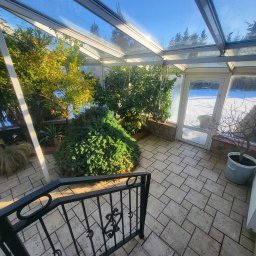 Krystian Lewandowski - Ogrzewany całoroczny ogród zimowy z cytrynowymi drzewkami, widok z góry schodów z czarną balustradą. Za szklanymi drzwiami śnieżny krajobraz.