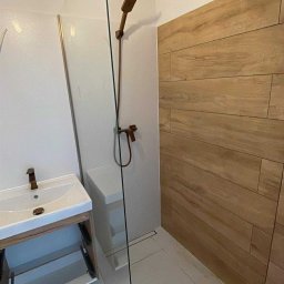 Usługi wykończeniowe Radoń - Nowoczesna łazienka z kabiną prysznicową typu walk-in, drewnopodobnymi płytkami na ścianie i umywalką z szafką. Armatura w kolorze miedzi.