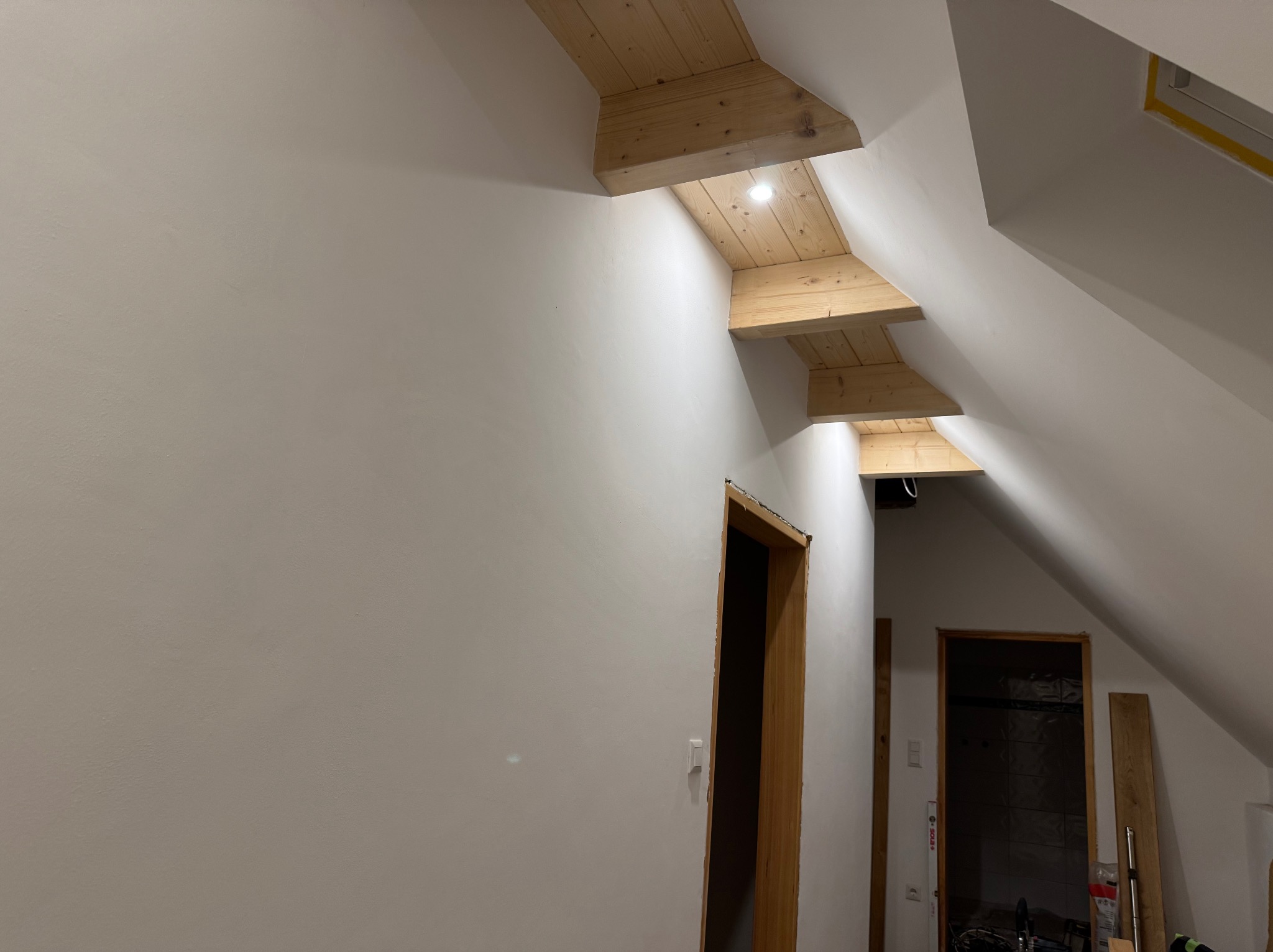 Poddasze po szpachlowaniu i malowaniu na biało, z drewnianymi elementami konstrukcyjnymi i otworami drzwiowymi. Widoczne ślady prac wykończeniowych.