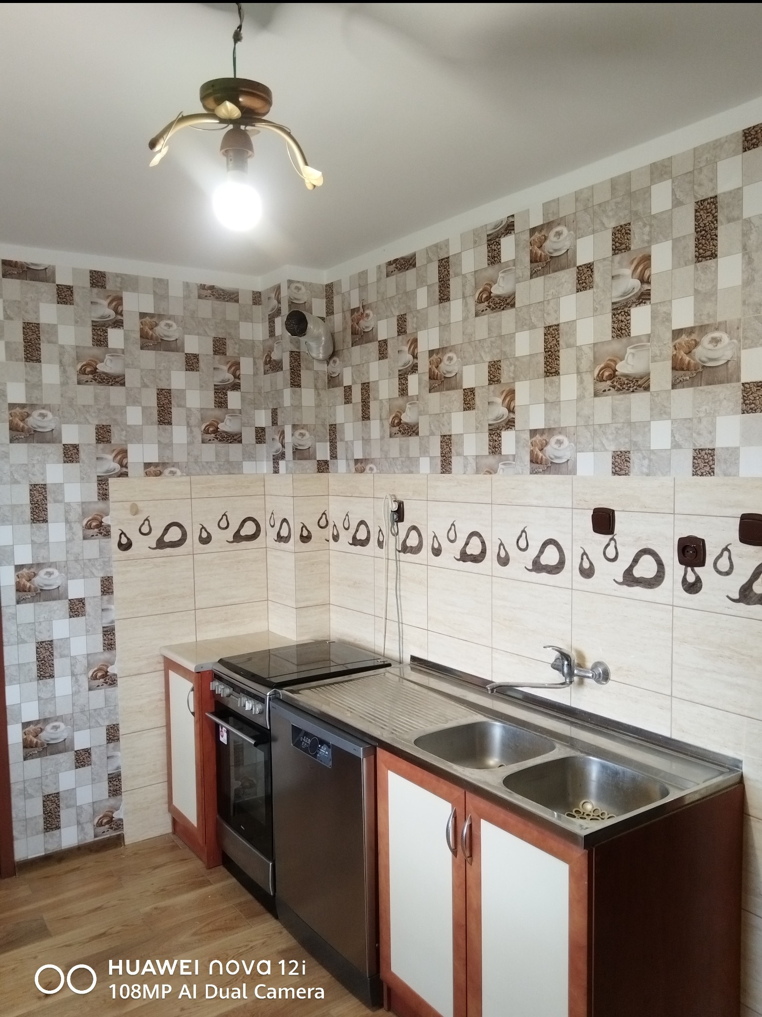 Wykończona kuchnia z płytkami w motywy kawowe i owocowe, zabudową kuchenną z dwukomorowym zlewem, piekarnikiem i płytą. Nietypowa lampa sufitowa.