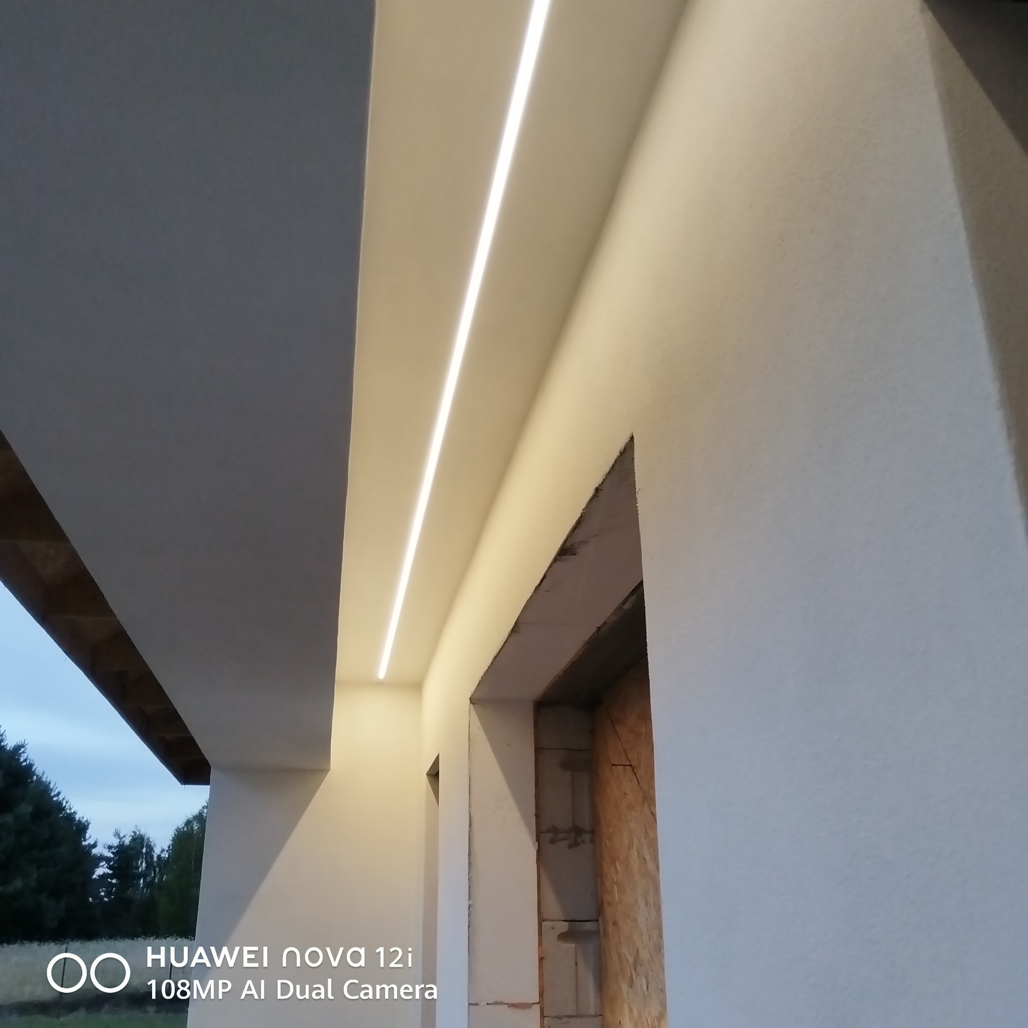 Nowoczesne oświetlenie LED wpuszczone w sufit podwieszany, widok z dołu. Ściany wykończone gładzią, surowy otwór drzwiowy w tle. Minimalistyczny design.