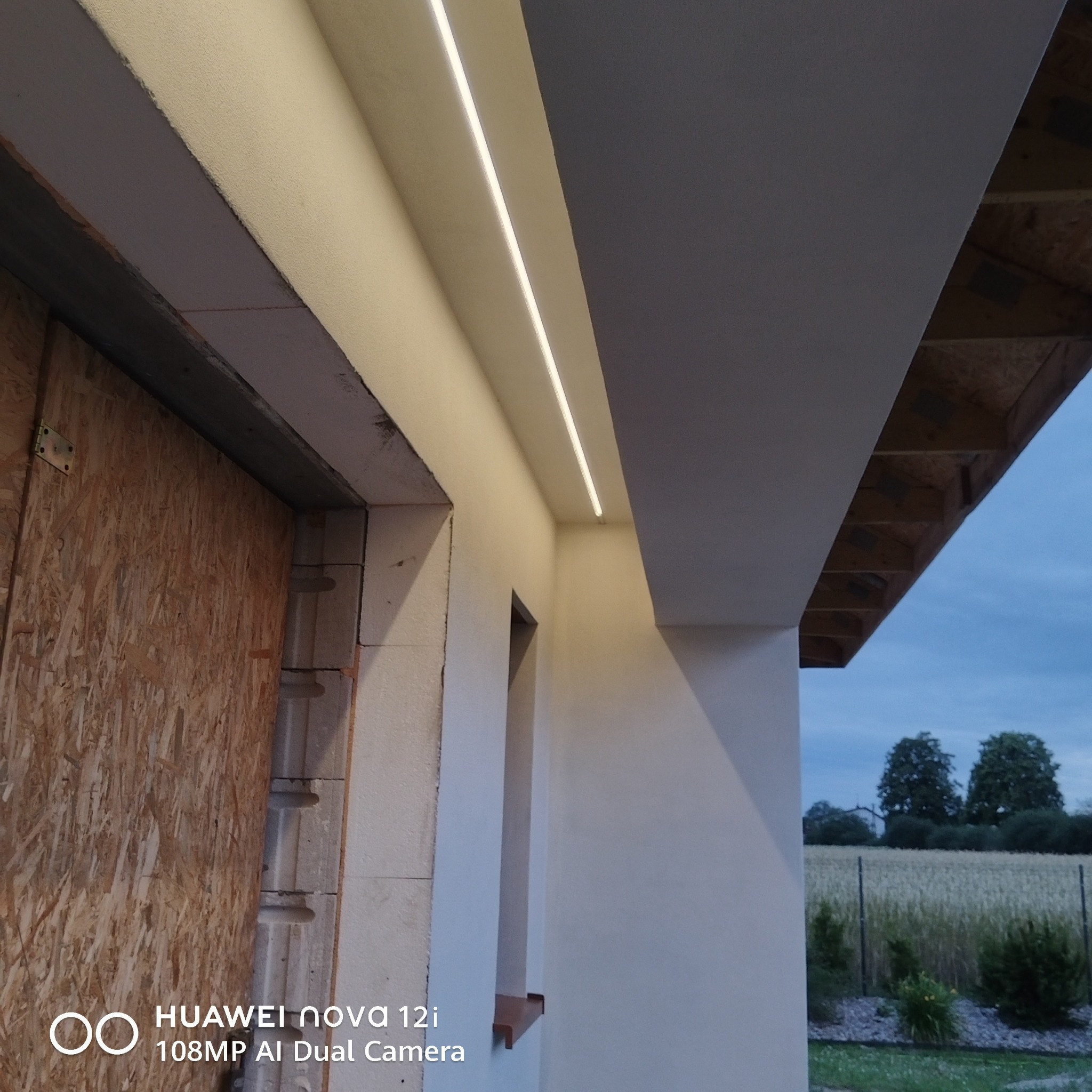 Nowoczesne oświetlenie LED w podbitce dachowej domu jednorodzinnego, widok z dołu. Elementy wykończeniowe w trakcie montażu, widoczne płyty OSB i bloczki.