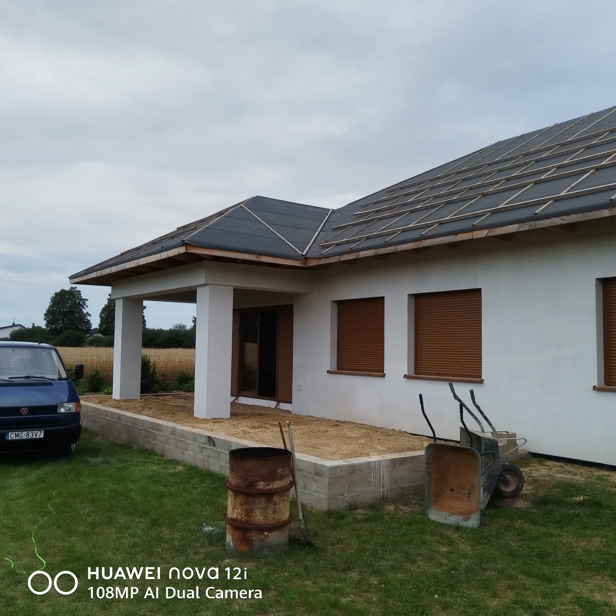 Dom jednorodzinny w trakcie prac wykończeniowych elewacji i dachu. Widoczne rusztowania, narzędzia i materiały budowlane. Ujęcie z zewnątrz, w dzień.