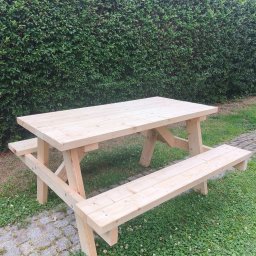 GranWood - Nowy, jasny drewniany stół piknikowy z ławkami, stojący na zielonym trawniku z koniczyną, obok brukowanej ścieżki, na tle gęstego żywopłotu.