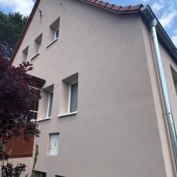 ELEVARO - Elewacja domu jednorodzinnego w odcieniach beżu, z widocznymi oknami, rynną i fragmentem dachu. Ujęcie z dołu, podkreślające strukturę tynku.