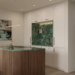 Martyna Koperska Wnętrza - Nowoczesna kuchnia z wyspą o zielonym blacie i ryflowanym wykończeniu. Białe szafki z miedzianymi uchwytami i zielony marmur na ścianie dodają elegancji.