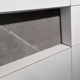 Baubarti - Białe, matowe płytki z wnęką wyłożoną szarą płytą imitującą marmur. Minimalistyczny design, precyzyjne fugi, nowoczesne wykończenie ściany.