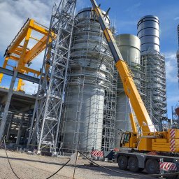 NDTEST - Konstrukcja stalowa w trakcie budowy z użyciem dźwigu, widoczne rusztowania i elementy spawane. Błękitne niebo w tle. Prace na wysokościach.