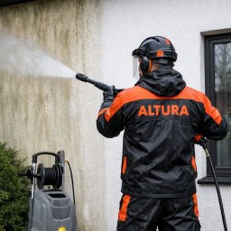 ALTURA - Pracownik w kombinezonie czyści elewację myjką ciśnieniową. Widoczny efekt czyszczenia: brudna i czysta część ściany. Na plecach napis ALTURA.