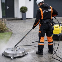 ALTURA - Pracownik w kombinezonie marki ALTURA czyści kostkę brukową za pomocą profesjonalnej myjki ciśnieniowej z okrągłą dyszą. Widoczny efekt czyszczenia.