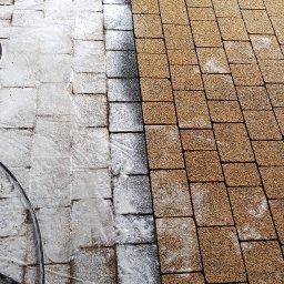 ALTURA - Częściowo umyta kostka brukowa w trakcie czyszczenia. Widoczna różnica między czystą, jasną powierzchnią a brudną, ciemniejszą. W tle fragmenty innych powierzchni.