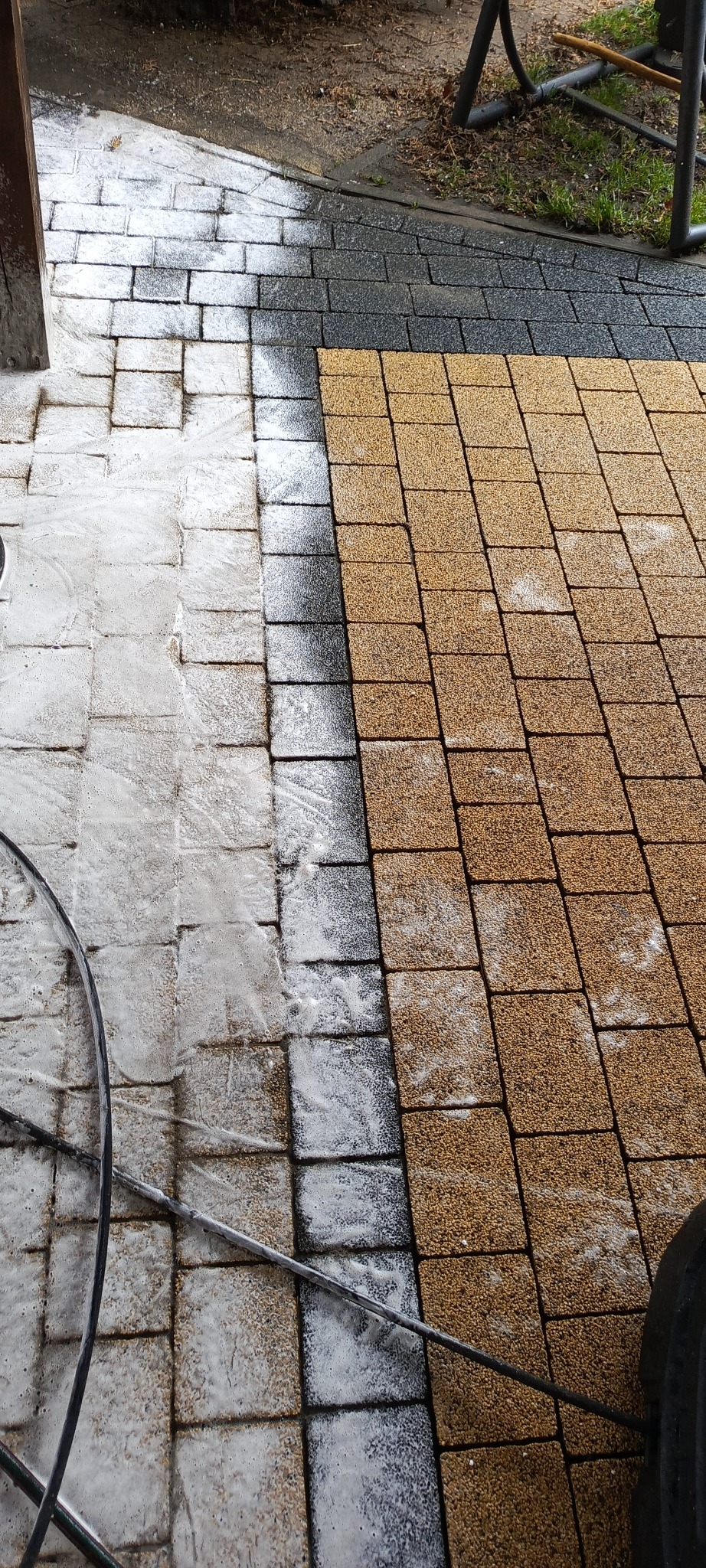 Częściowo umyta kostka brukowa w trakcie czyszczenia. Widoczna różnica między czystą, jasną powierzchnią a brudną, ciemniejszą. W tle fragmenty innych powierzchni.