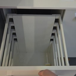 Jakub Zajac - Otwarta, biała szuflada z systemem organizacji wewnętrznej. Widoczny fragment dłoni otwierającej szufladę. Minimalistyczny design, jasne oświetlenie.