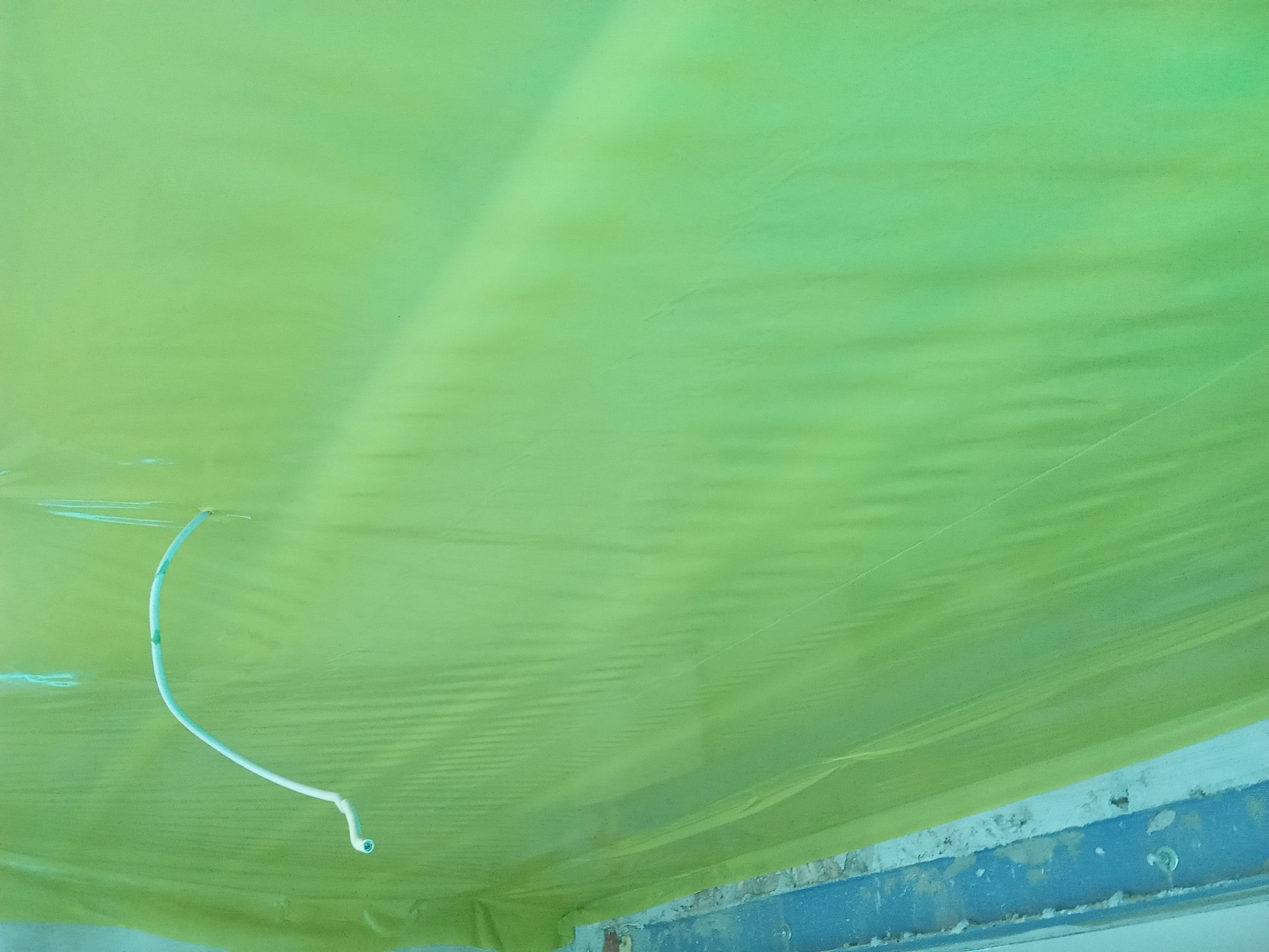 Zabezpieczona folią malarską sufitowa powierzchnia z wystającym przewodem elektrycznym, przygotowana do prac wykończeniowych.