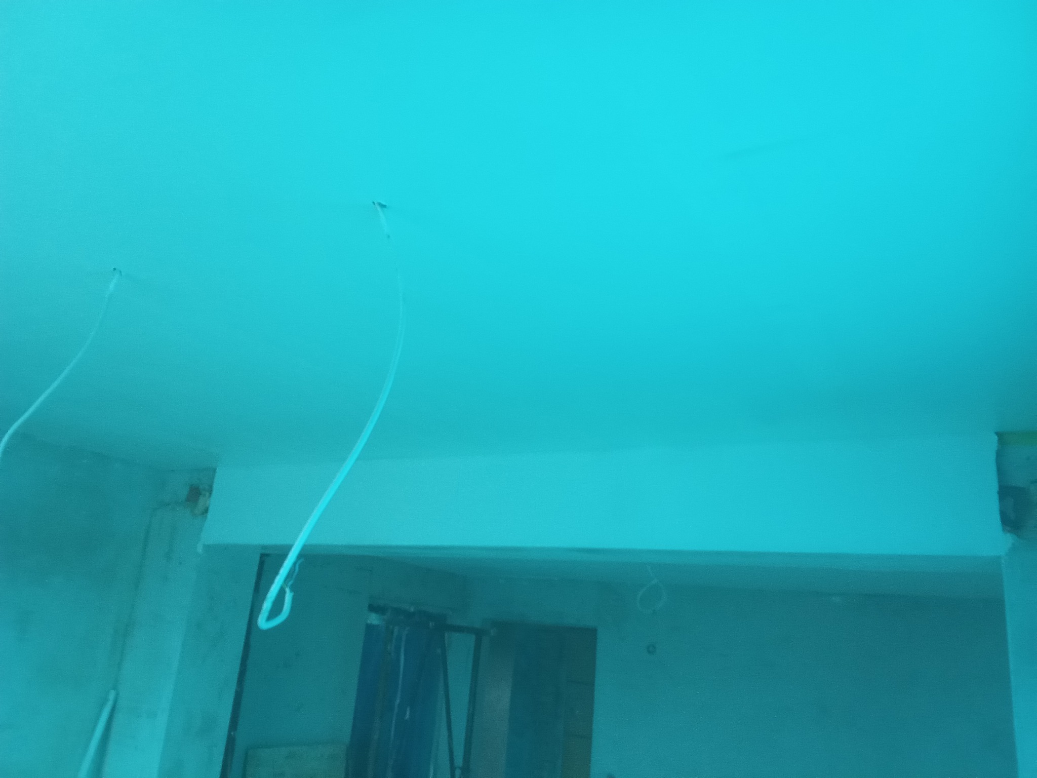 Niebieskie wnętrze w trakcie remontu. Widoczne kable wystające z sufitu i fragment ściany z widocznymi niedoskonałościami. Prace przygotowawcze przed malowaniem.