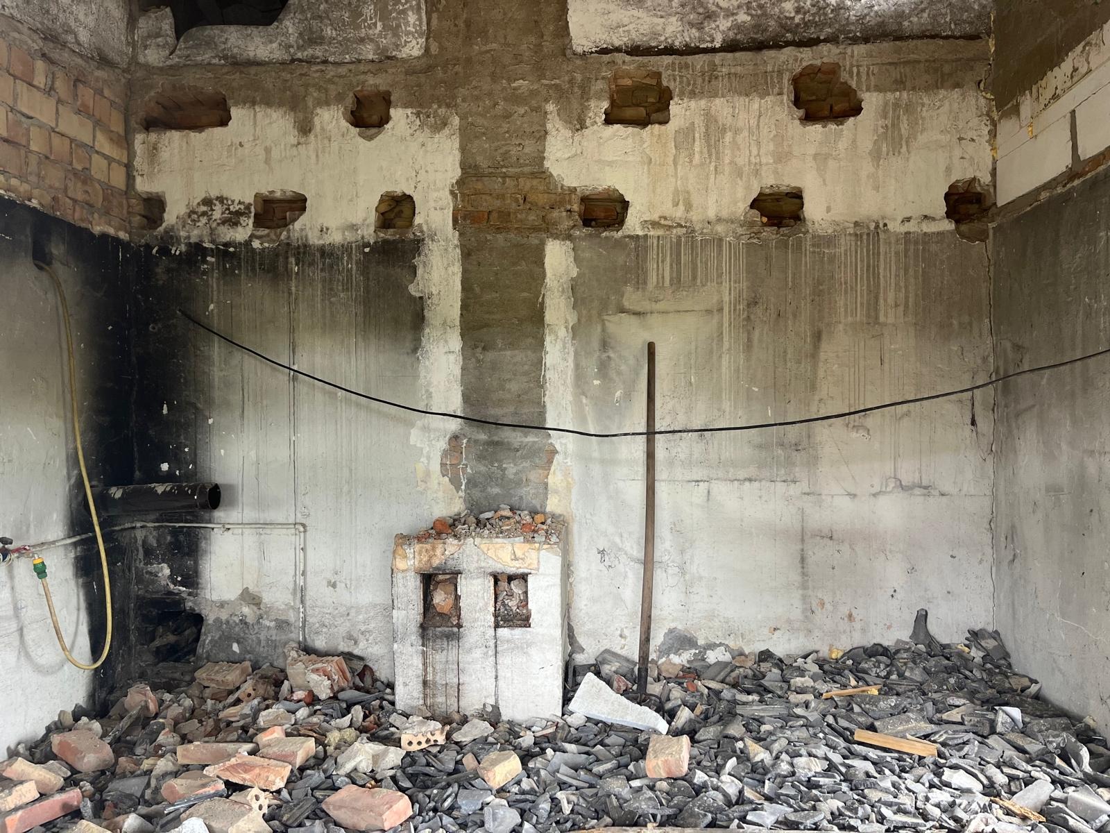 Wnętrze w trakcie demontażu: odsłonięte cegły, resztki tynku, gruz na podłodze. Widoczne ślady po instalacjach i otworach w ścianach. Surowy stan przed remontem.