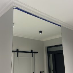 Łukasz Grzelak - Nowoczesne wnętrze z dużym lustrem, odzwierciedlającym drzwi przesuwne w stylu stodoły i minimalistyczne oświetlenie sufitowe. Widoczne listwy dekoracyjne.