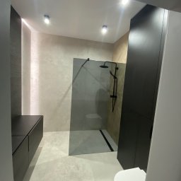 Łukasz Grzelak - Nowoczesna łazienka z kabiną typu walk-in, czarną armaturą i szafkami w kolorze antracytu. Jasne płytki podłogowe i ścienne tworzą spójną całość.