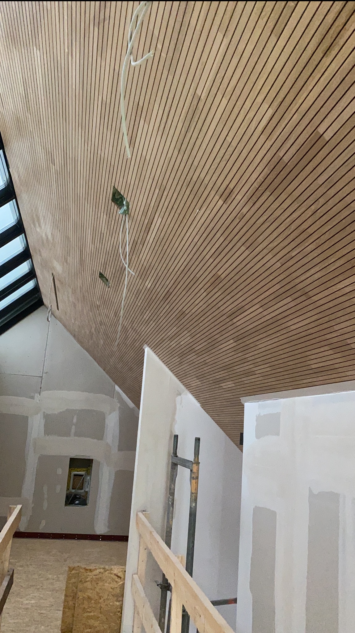 Drewniana boazeria na skośnym suficie poddasza z widocznymi przewodami elektrycznymi, ściany w trakcie szpachlowania, okno dachowe w lewym górnym rogu.