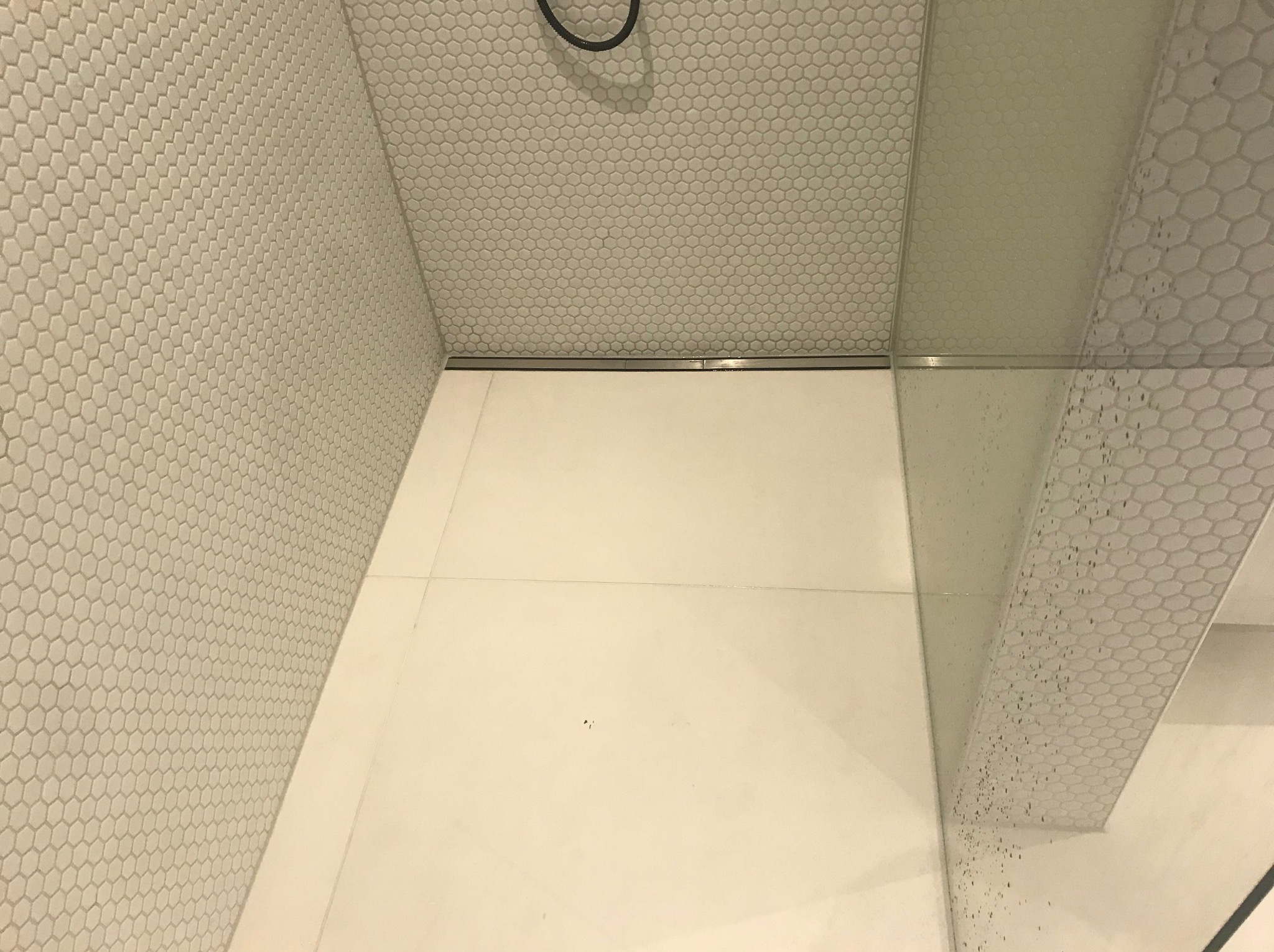 Biała łazienka z heksagonalnymi płytkami na ścianach i podłodze, kabina prysznicowa ze szklaną ścianką. Minimalistyczny design, widok z góry.