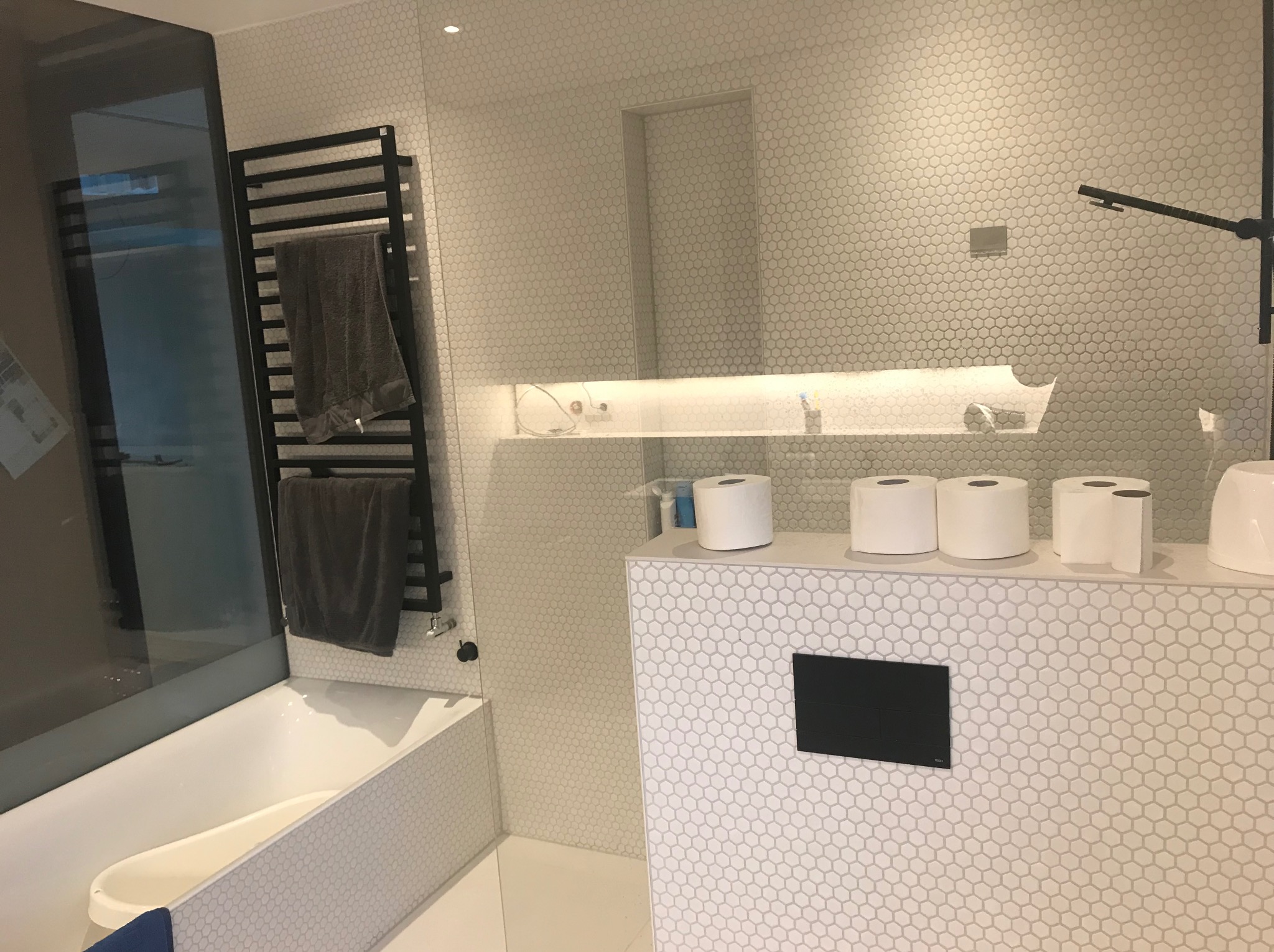 Nowoczesna łazienka w Kołbaskowie z białą mozaiką heksagonalną, czarnym grzejnikiem drabinkowym i szklaną kabiną prysznicową. Minimalistyczny design.