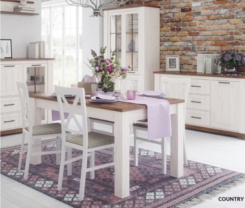 Jadalnia w stylu rustykalnym: białe meble z drewnianymi blatami, ceglana ściana w tle, kwiaty i dywan w etniczne wzory. Aranżacja wnętrza z szafkami i stołem.