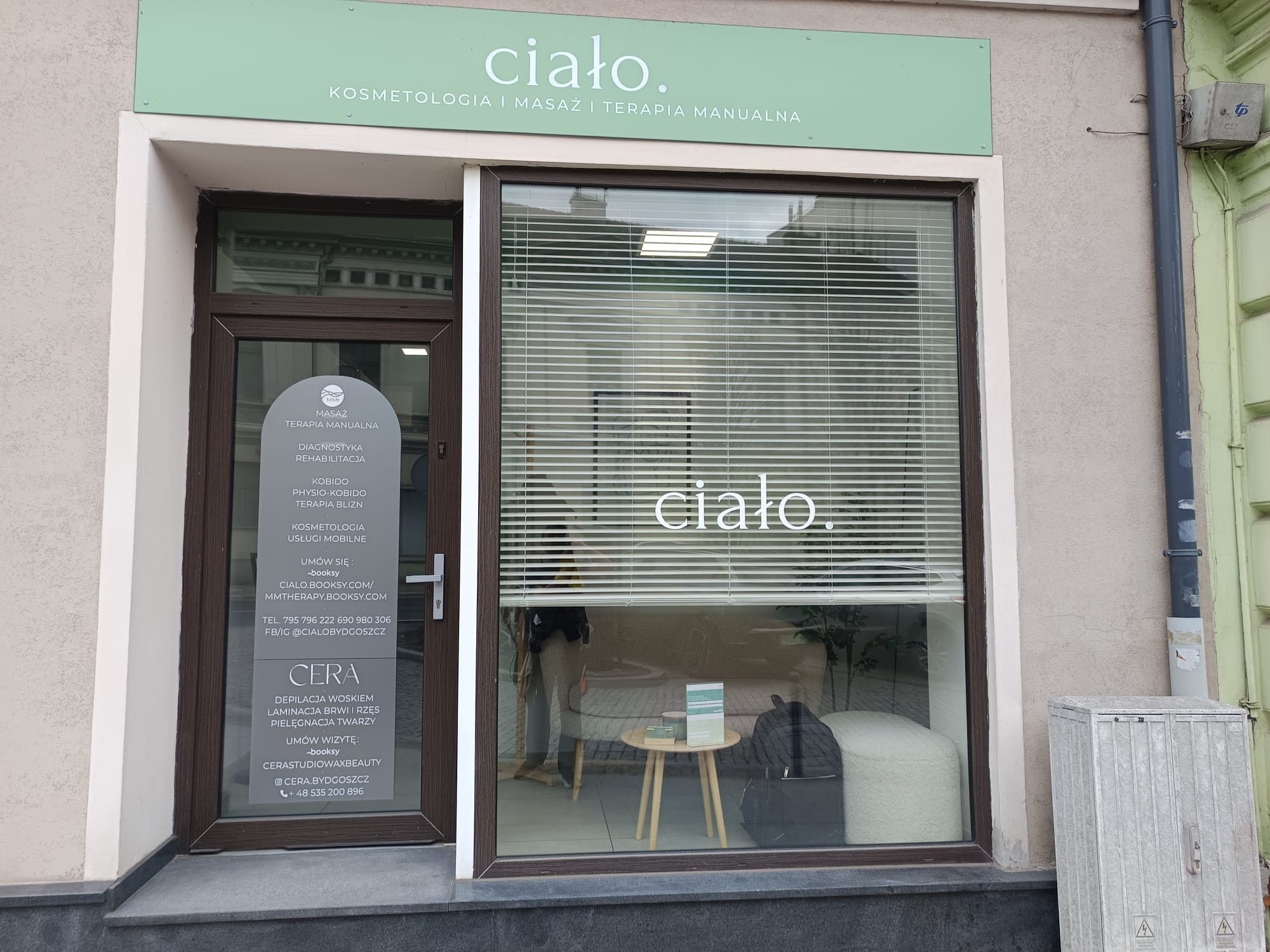 Fasada salonu kosmetycznego 'ciało.' z witryną, na której widnieje nazwa i oferta zabiegów. Widoczne rolety w oknach i informacje o depilacji 'CERA' na drzwiach.