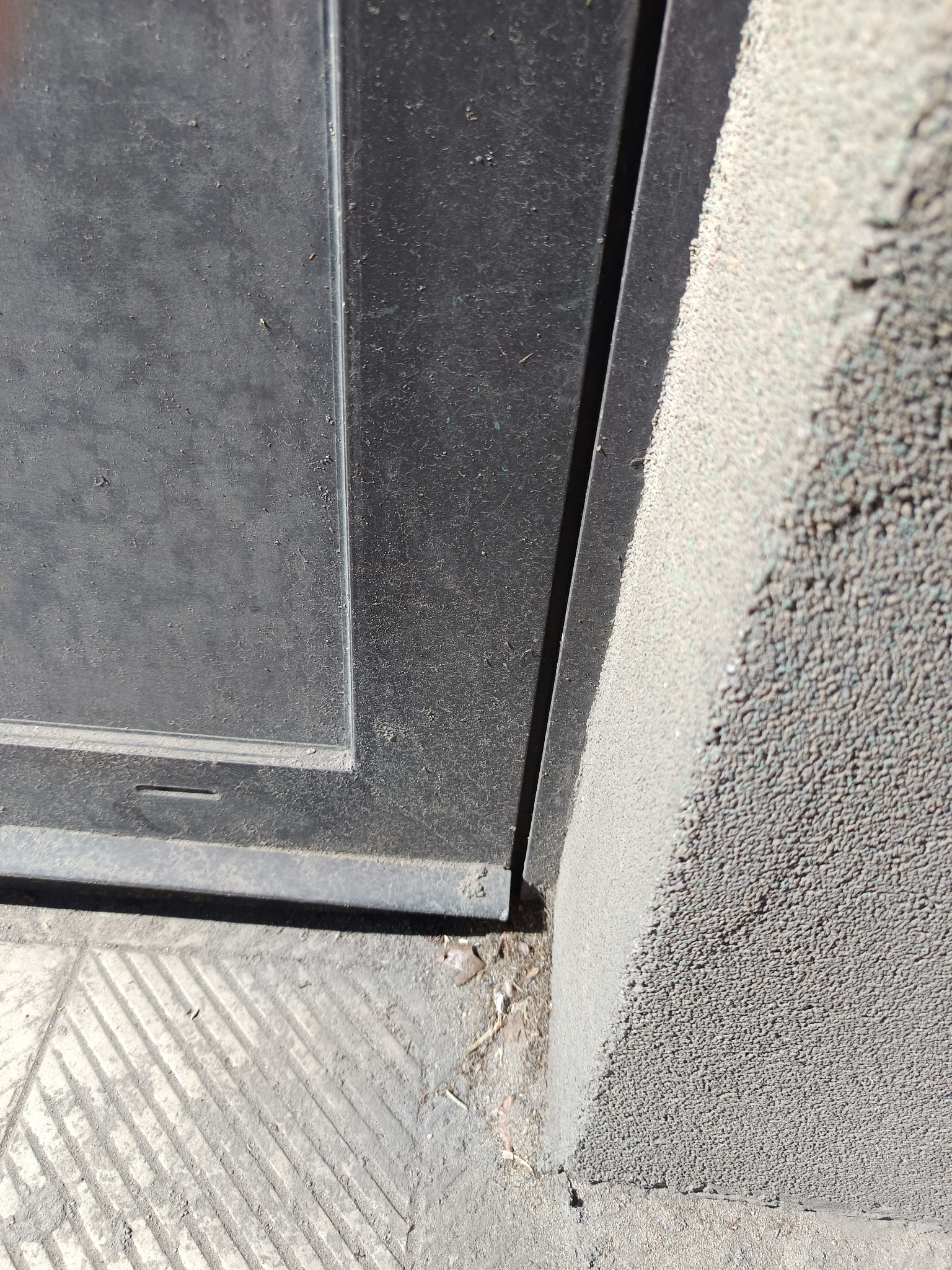 Brudne okno z ramą, zanieczyszczony parapet i chodnik przed budynkiem. Widoczne ślady kurzu i pyłu na powierzchniach.