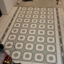 Mixbud - Ułożona podłoga z płytek w stylu retro, z widocznymi narzędziami i torbą monterską w rogu. Częściowo wykończona powierzchnia podłogi w pomieszczeniu.
