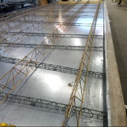 FIRMA BUDOWLANA MARITIME - Metalowa forma z ułożonym zbrojeniem, przygotowana do zalania betonem. Widoczne elementy konstrukcyjne i detale łączeń. Ujęcie z góry, oświetlenie przemysłowe.