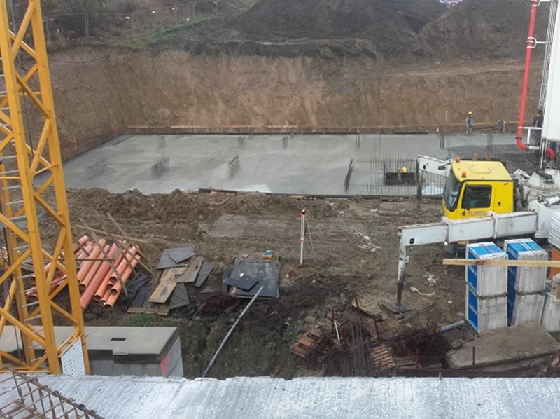 Wylany fundament zbrojony w Bąkowie, widok z góry. Żuraw budowlany i maszyna do betonu na placu budowy. Wykop pod fundament zabezpieczony.