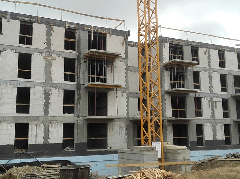 Wznoszenie wielopiętrowego budynku z betonu komórkowego. Widoczne szalunki balkonowe i żuraw budowlany. Etap murowania ścian i przygotowania do wylewania stropów.